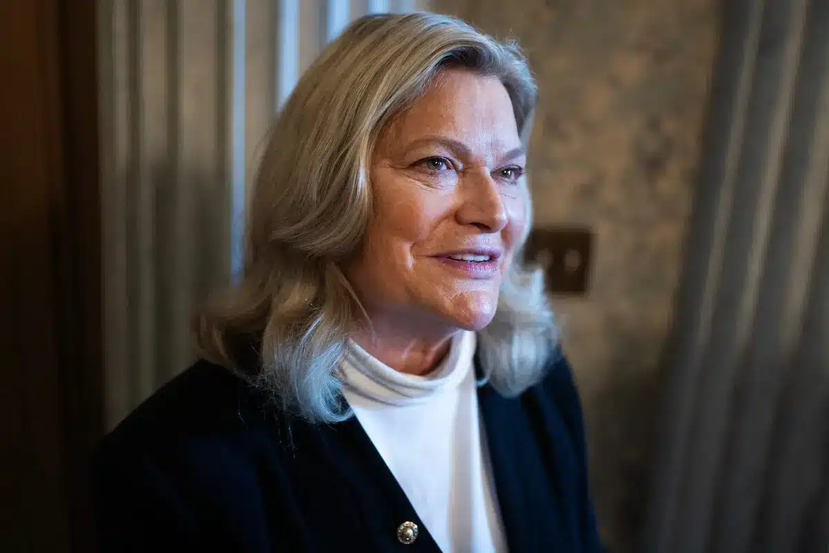 Close-up of Senator Cynthia Lummis smiling, wearing a dark jacket, with soft lighting.